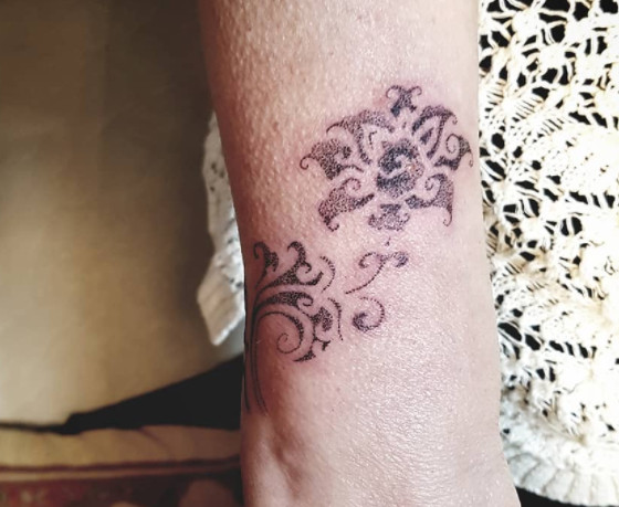 An ornamental black dotwork floral tattoo design on a wrist.