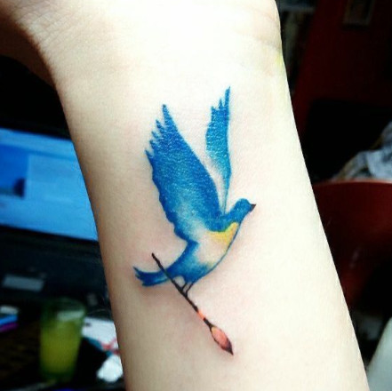 A bright watercolor bluebird tattoo with a yellow belly on a wrist.