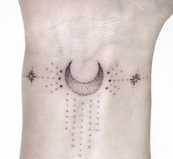 A delicate dotwork geometric moon tattoo with dripping stars on a wrist.