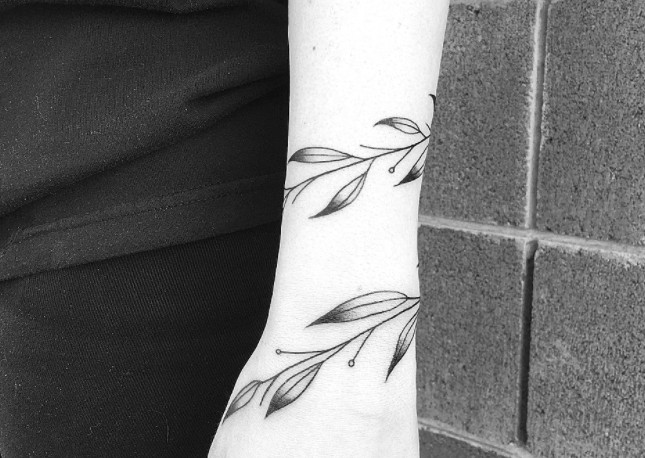 A vine of leaves tattoo wrapping around a wrist in black ink.