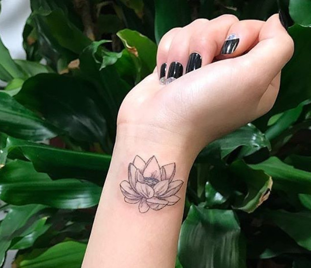 A lotus flower tattoo with fine line art details on a wrist.