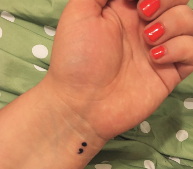 A minimalist semicolon tattoo on a wrist.