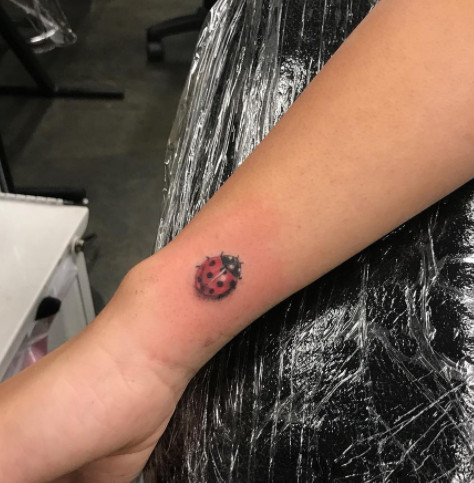 A red ladybug tattoo with black spots on a wrist.