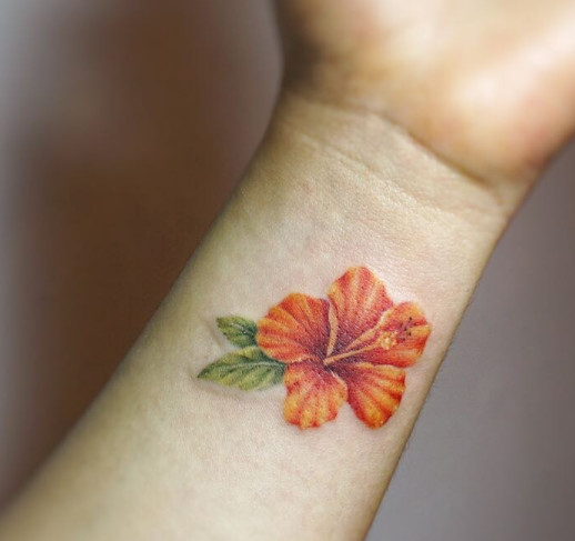 A bright orange hibiscus flower tattoo with minimal black ink on a wrist.