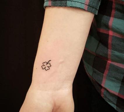 A simple black outline shamrock tattoo on a wrist.