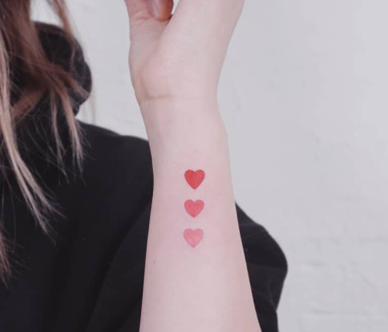 Three small red ombré heart tattoos fading in color on a wrist.