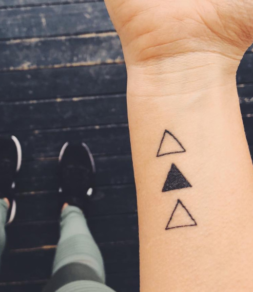 Three minimalist black triangle tattoos on a wrist.