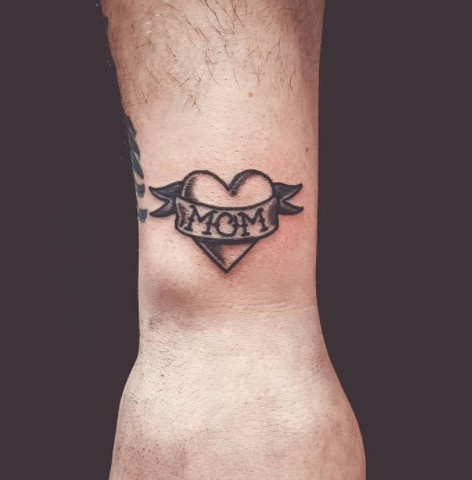 A traditional American tattoo style &quot;Mom&quot; heart tattoo on a wrist.