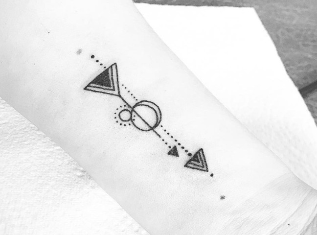 Geometric black arrow tattoos with dotwork details on a wrist.