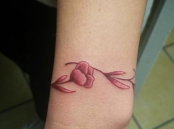 An ombré floral wristlet tattoo in red and pink shades wrapping around a wrist.