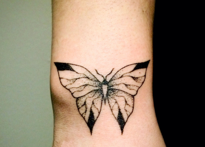 A black and white butterfly tattoo on a wrist.