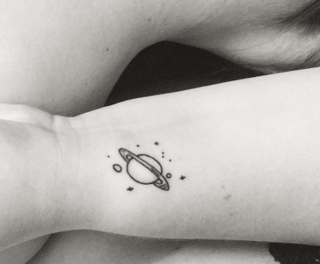 A small black ink space scene tattoo on a wrist.