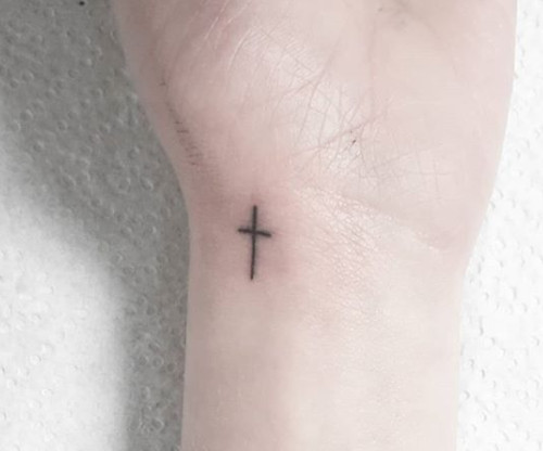 A tiny black cross tattoo on the inside of a wrist.