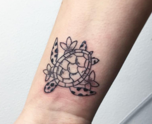 A turtle tattoo surrounded by flowers on a wrist.