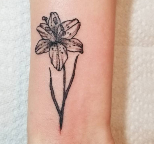 A small black and white lily flower tattoo on a wrist.