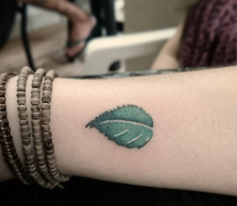 A small green leaf tattoo with shaded details on a wrist.