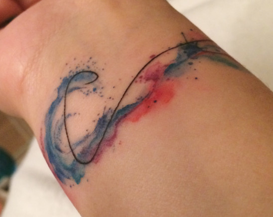 A colorful watercolor wave tattoo splashing on a wrist.