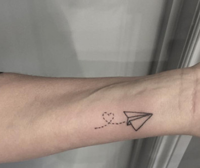 A simple black paper plane tattoo on a wrist.