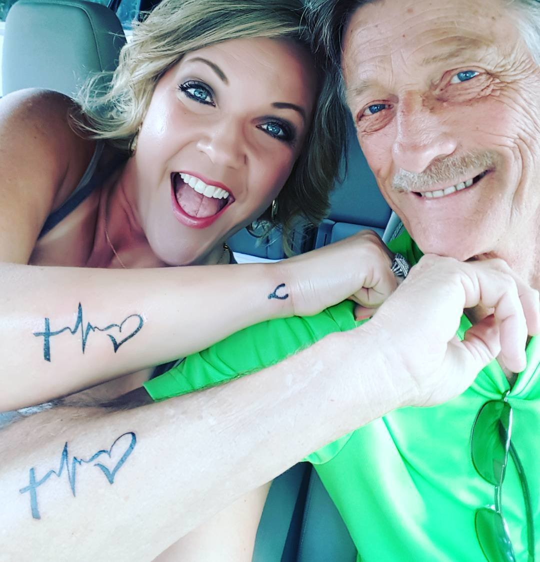 Father and daughter showing forearm tattoos of lifeline electrocardiogram patterns, symbolizing their enduring support for each other through life's ups and downs.