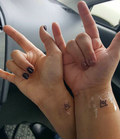 Heart-shaped rocker hand symbol tattoos, representing shared music taste and passionate friendship