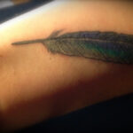 Single black feather tattoo on forearm