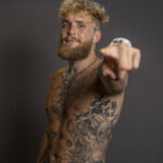 Jake Paul shirtless, pointing to the camera, showcasing his chest tattoos