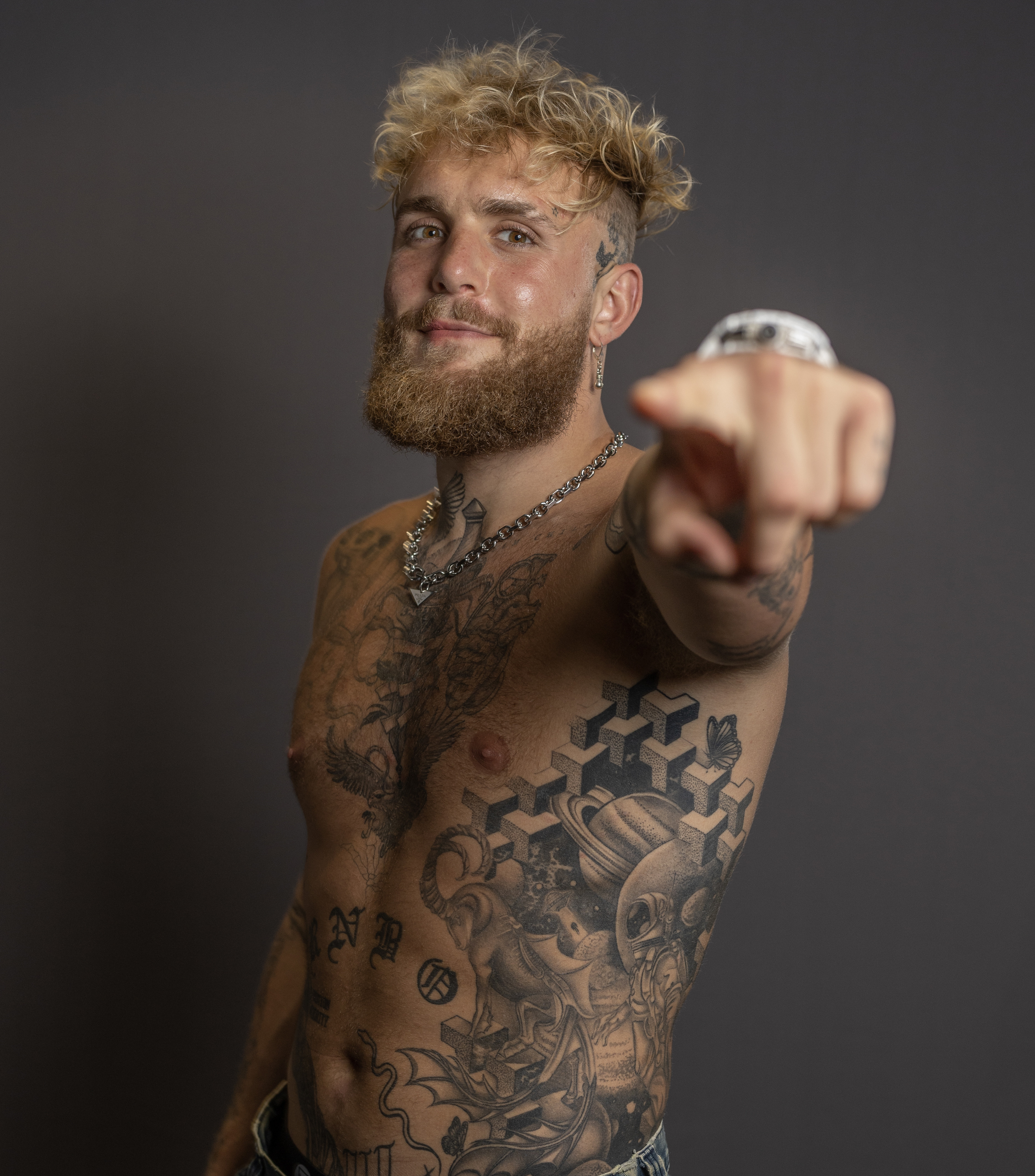 Jake Paul shirtless, pointing to the camera, showcasing his chest tattoos