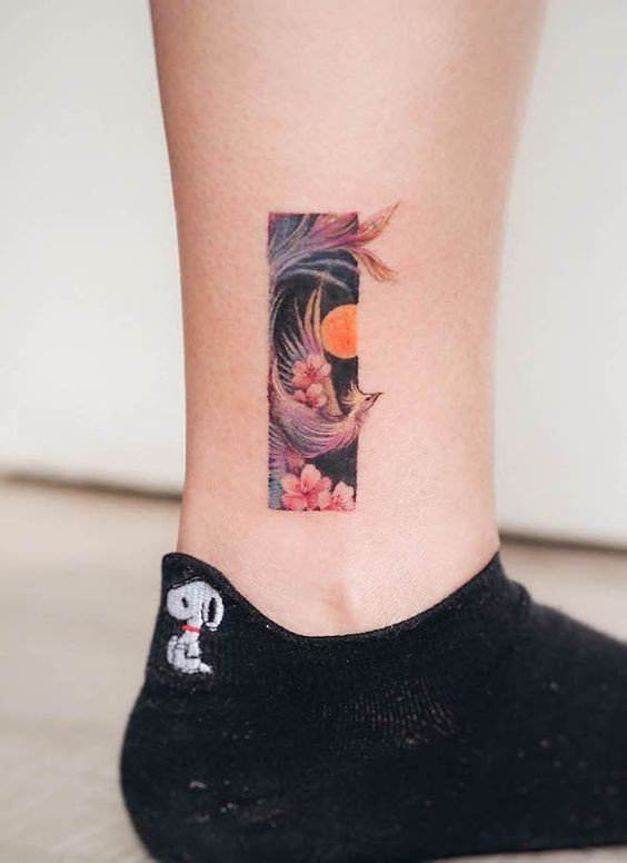 Colorful rectangle tattoo with a bird and flowers on a leg. Snoopy sock visible.