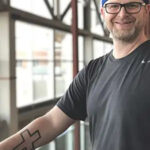 Jon Caldwell showing his forearm tattoo of a cross