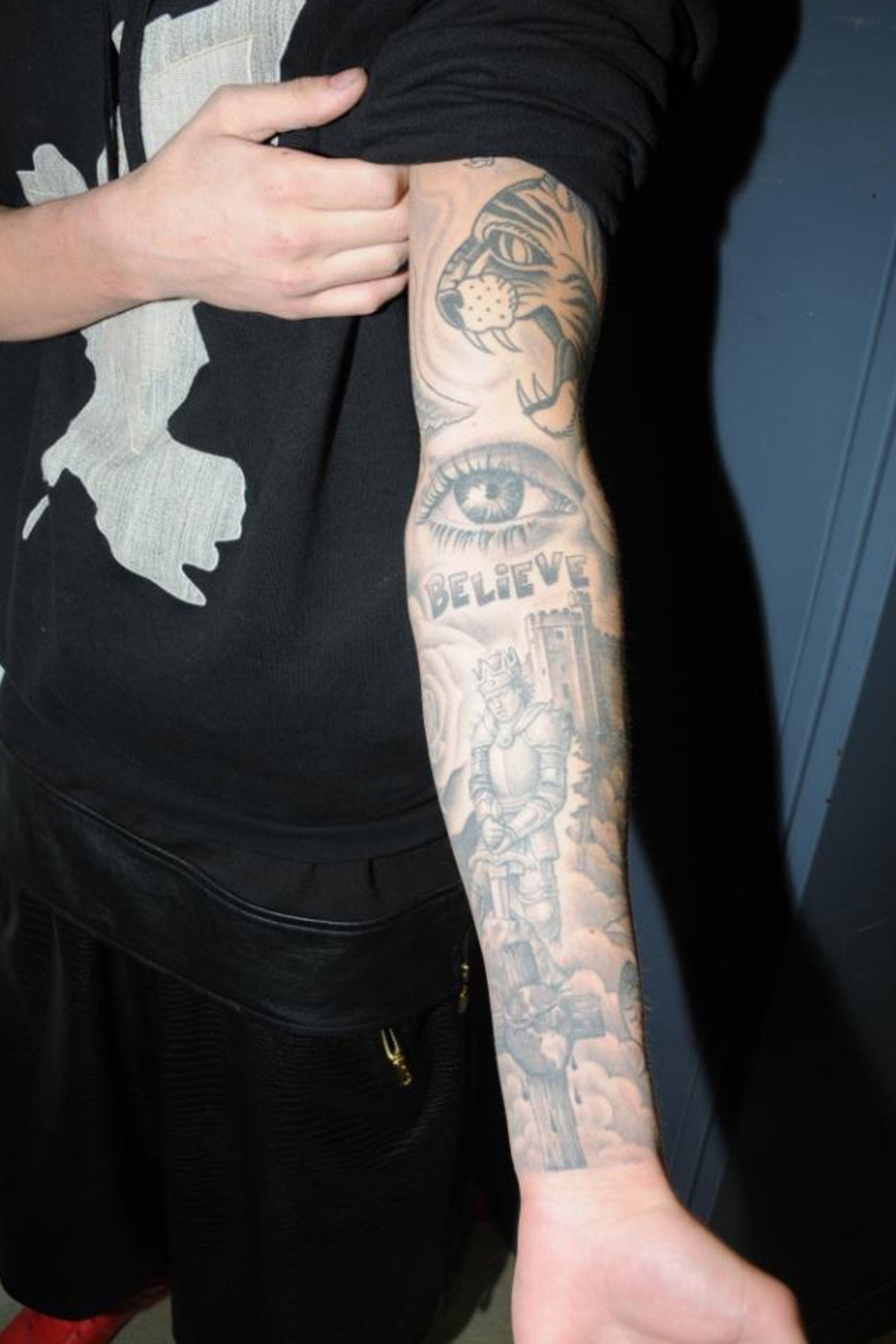 Justin Bieber sleeve tattoo with mom's eye, tiger, castle and knight, reflecting family and personal symbols.