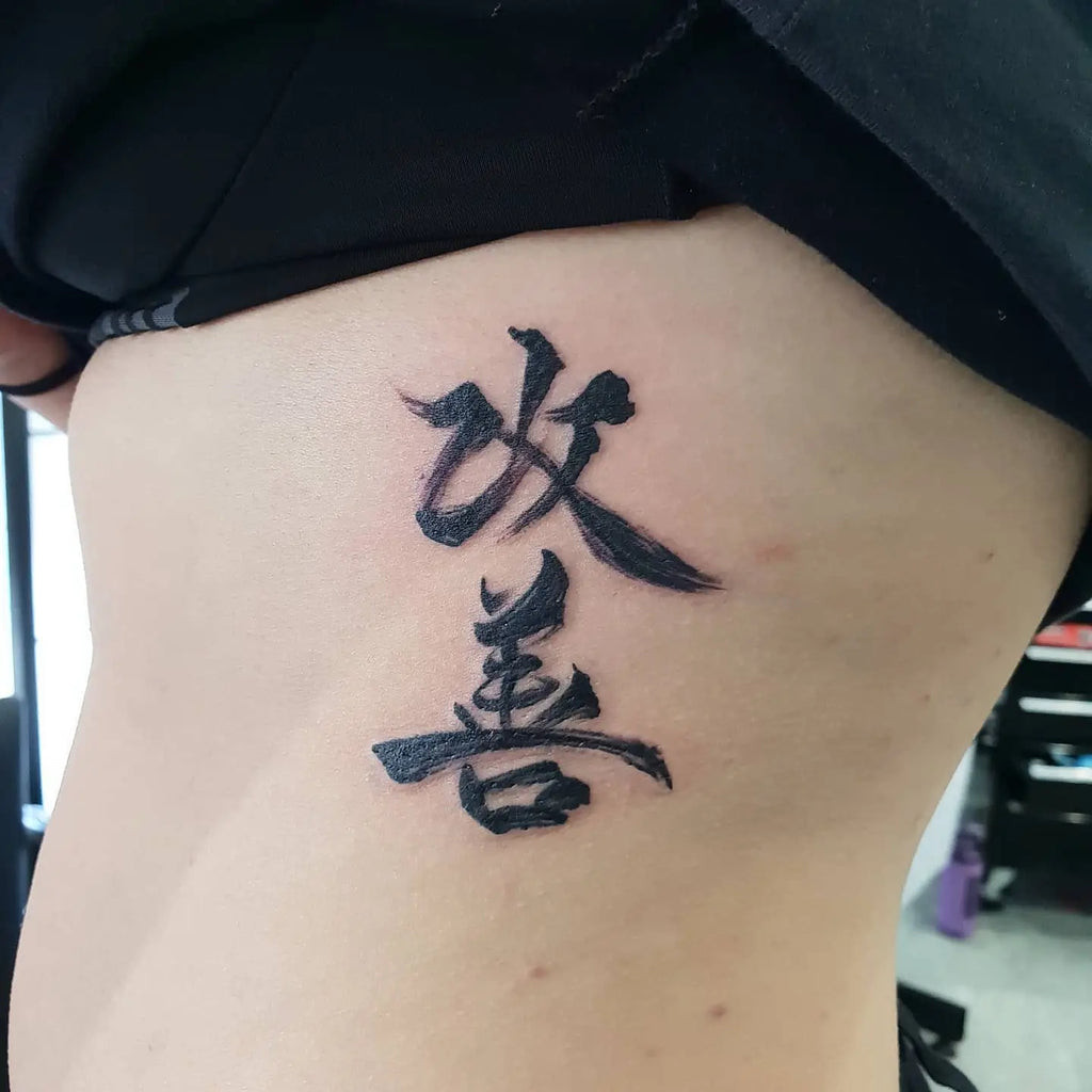 Elegant Kaizen script tattoo in black ink flowing across the collarbone, a subtle reminder of lifelong improvement