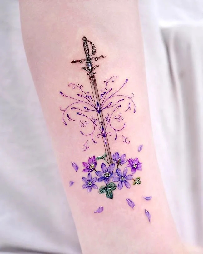 alt text: Floral knight sword tattoo on forearm, symbolizing feminine strength, self-protection, and inner guardian spirit