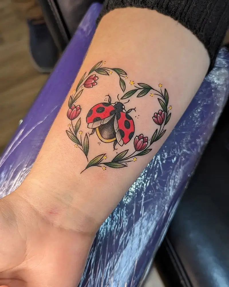 A ladybug tattoo combined with delicate floral accents, created by Bitchcrafttattoos