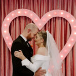 bride and groom touch foreheads in front of pink heart before going to Downtown Tattoo shop