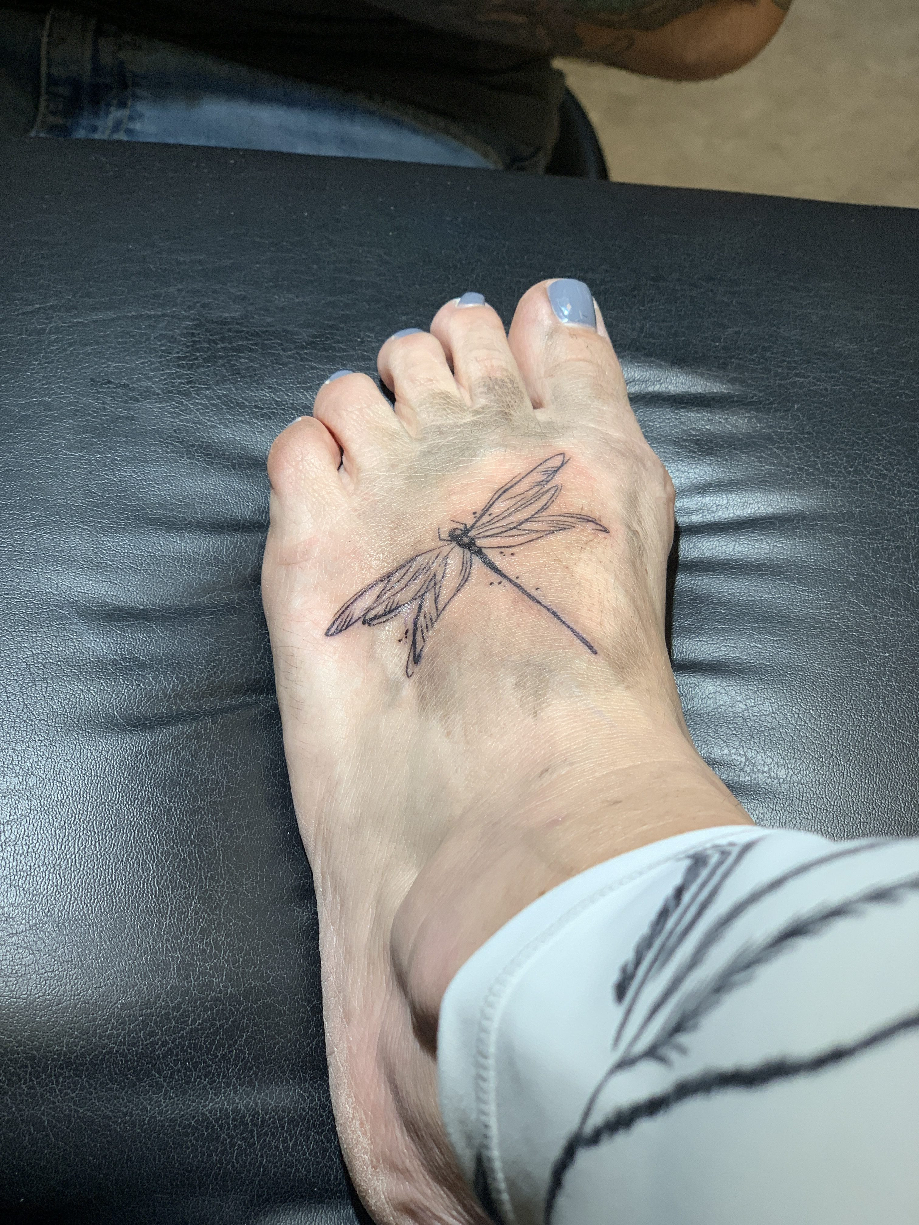 The outline of a dragonfly tattoo on a mother's foot, highlighting the detailed linework of the design.