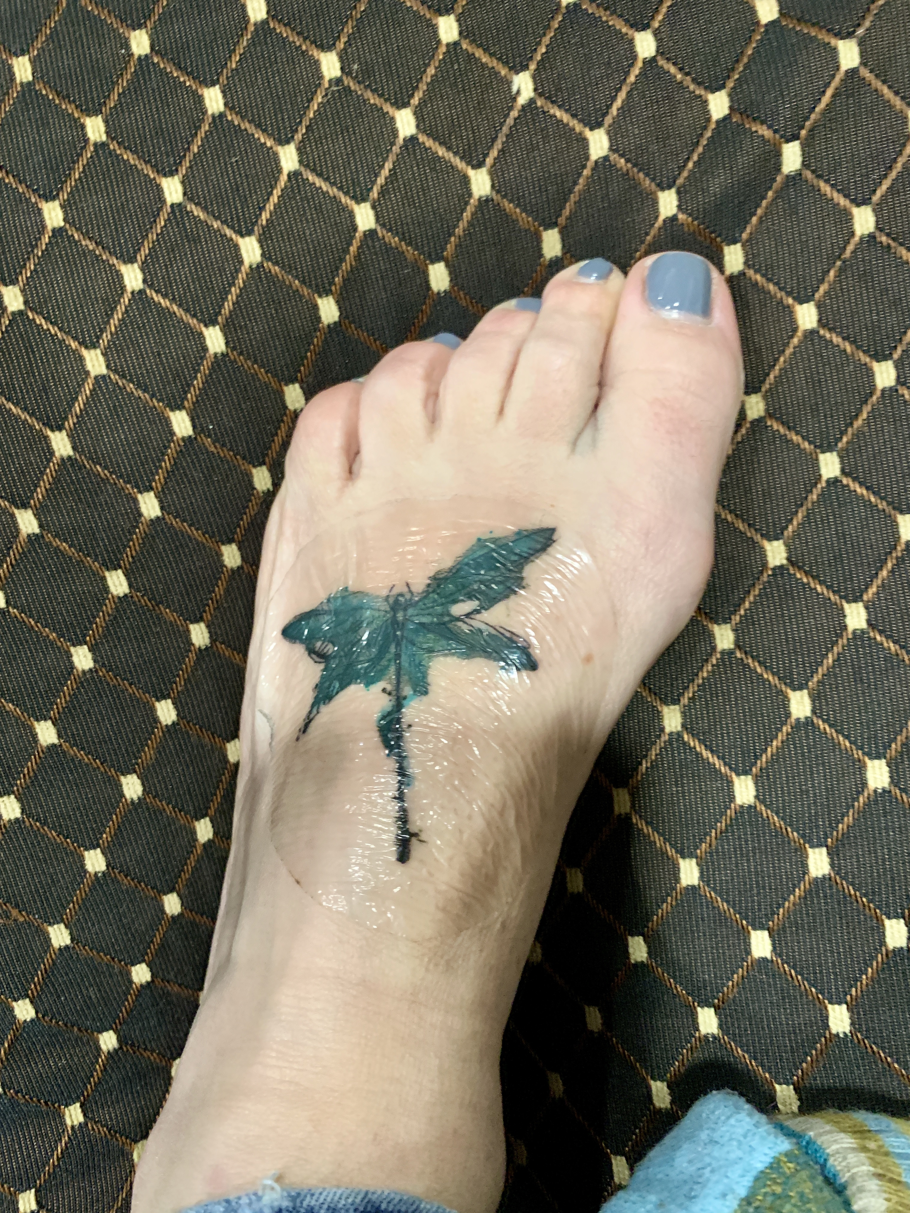 A healed watercolor dragonfly tattoo on a mother's foot, showcasing the soft hues and delicate details of the finished artwork.