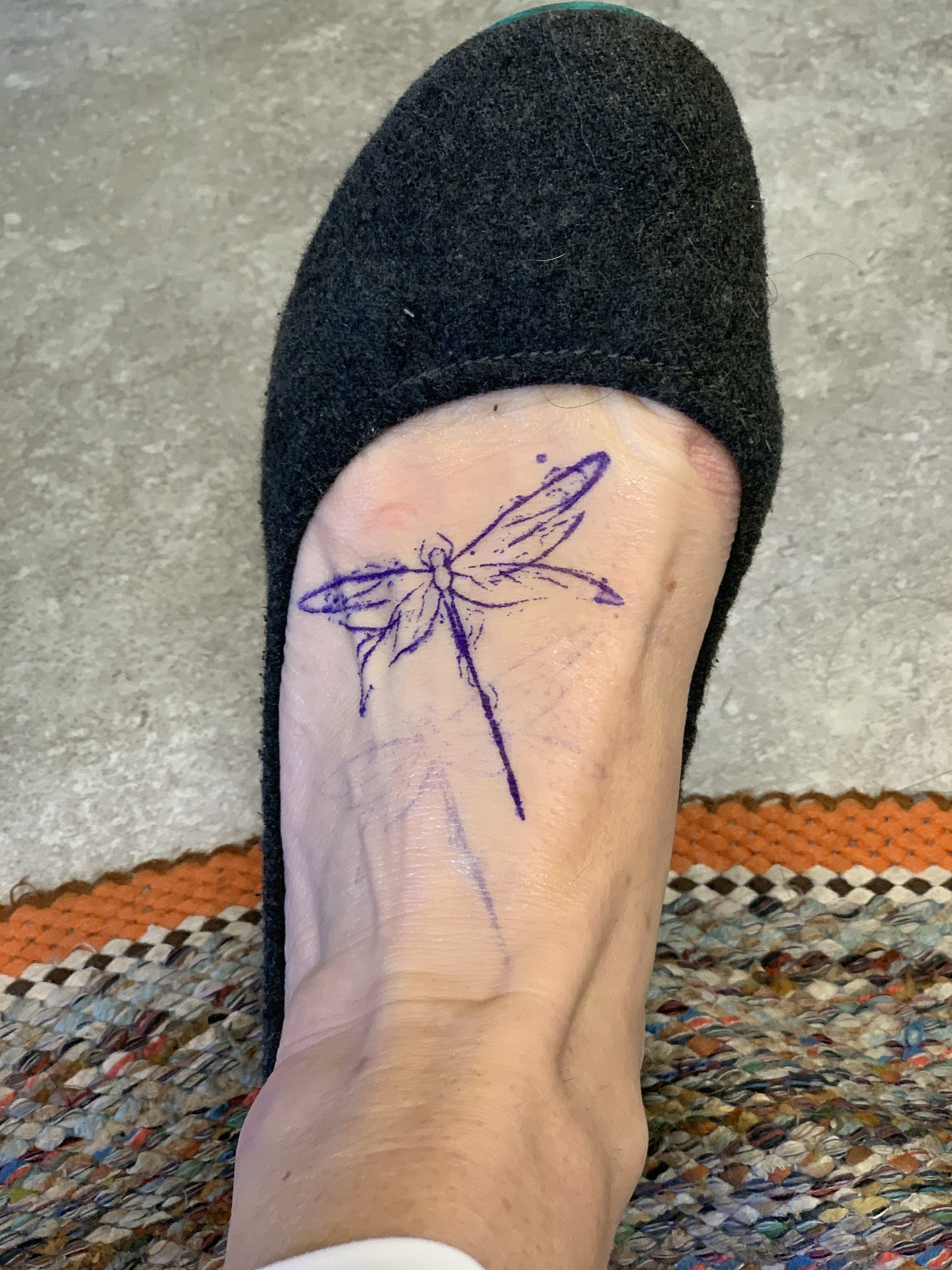 A mother adjusting the placement of a dragonfly tattoo stencil on her foot, ensuring it aligns perfectly with her style and comfort.