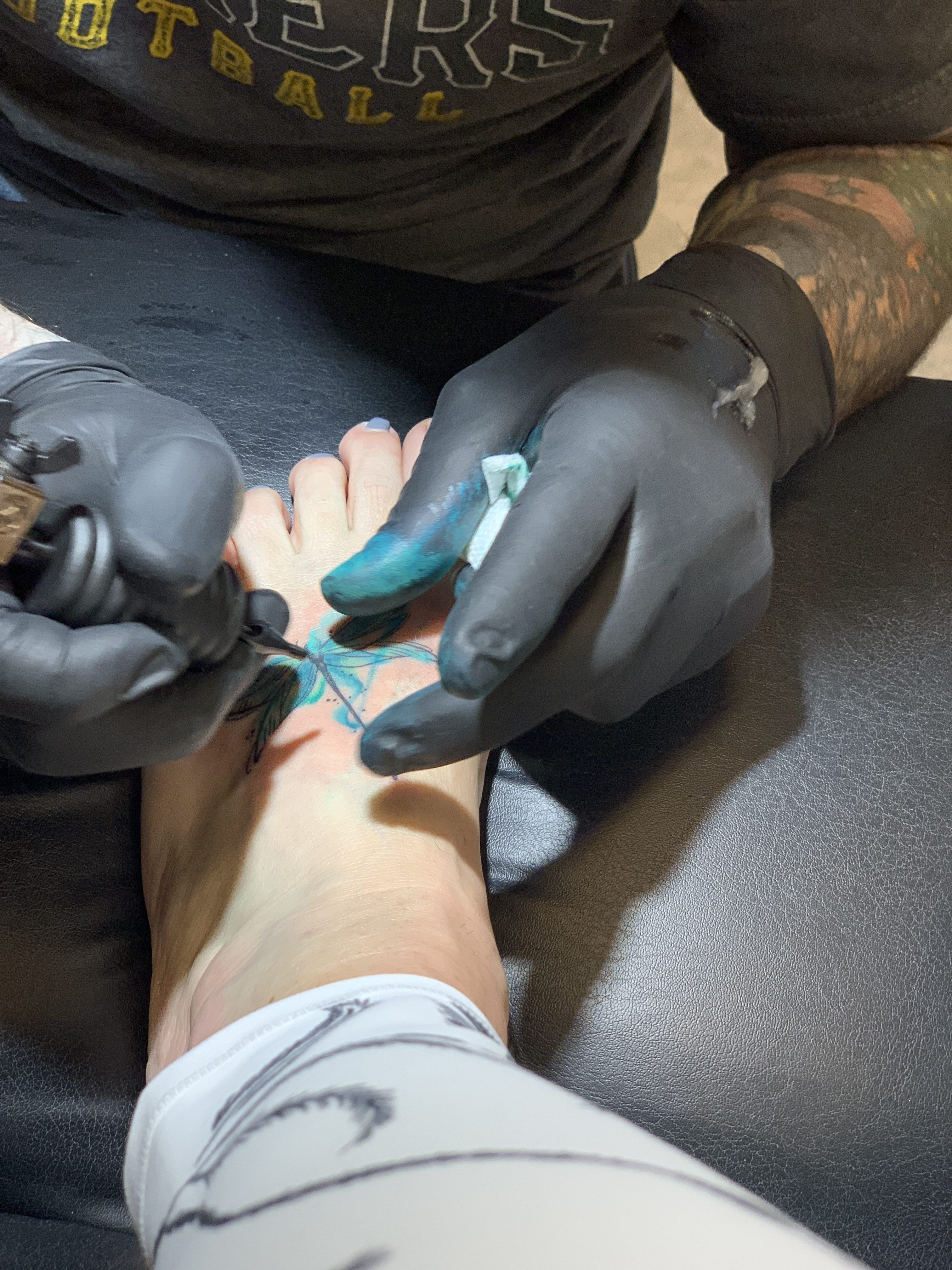 A tattoo artist carefully adding watercolor hues to a dragonfly tattoo, bringing the design to life with vibrant colors.