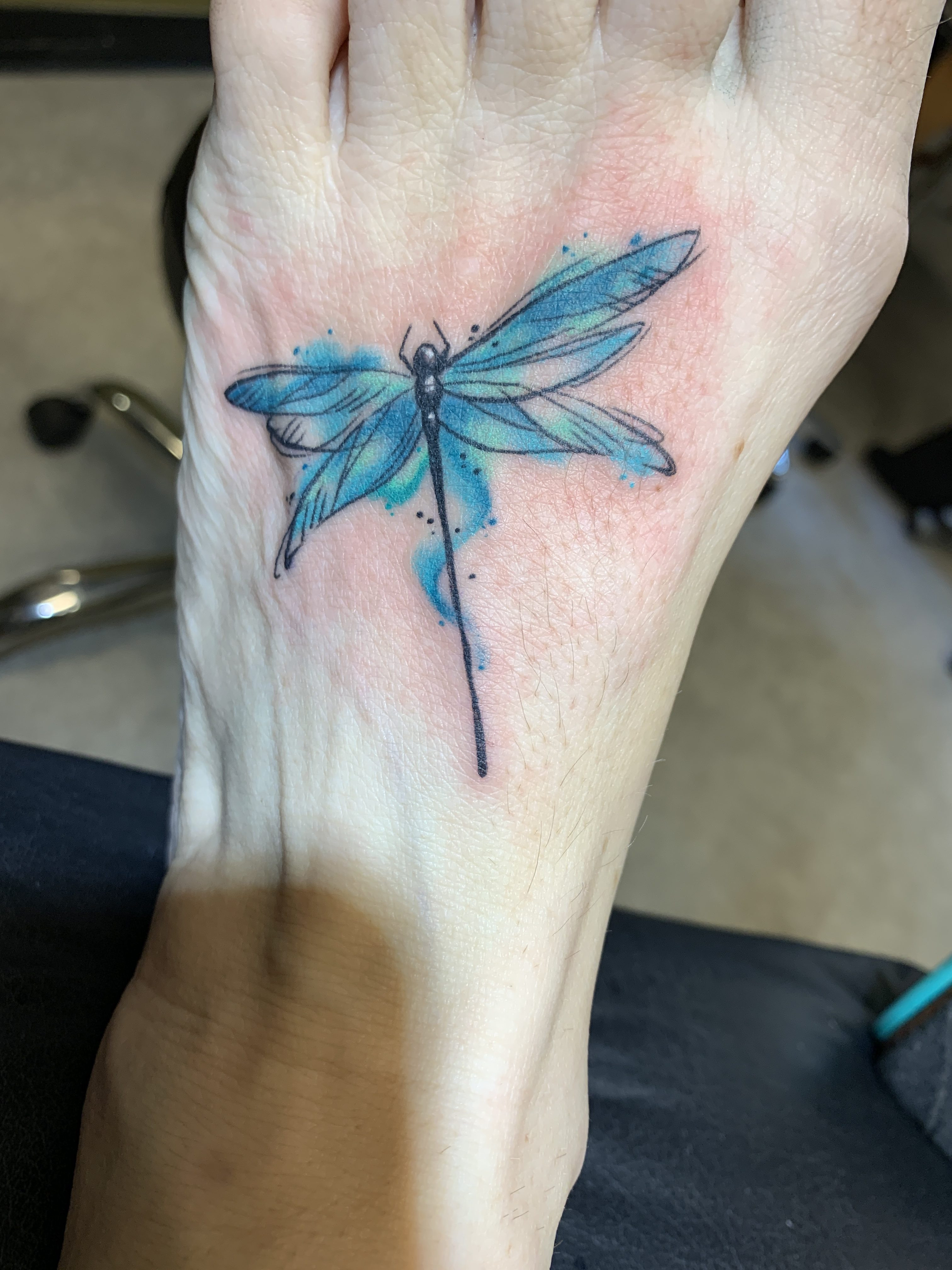 The vibrant watercolor details being applied to a dragonfly tattoo, showcasing the artistic skill and precision of the tattoo artist.