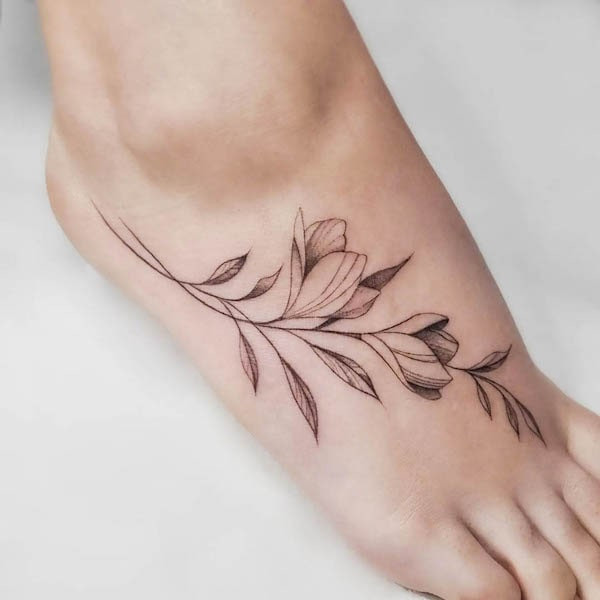 Leaves and branch foot tattoo, a natural and flowing design extending along the foot