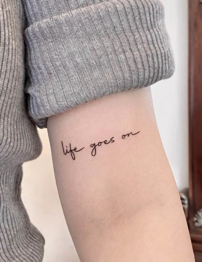 alt text: Delicate &quot;Life Goes On&quot; script tattoo on ankle, symbolizing resilience and a positive outlook on life