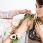 Close-up shot of a floral tattoo on a model's arm featuring purple, pink, and white flowers