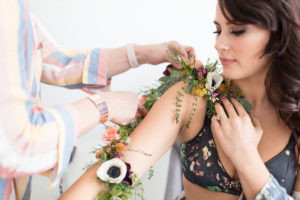 Close-up shot of a floral tattoo on a model's arm featuring purple, pink, and white flowers