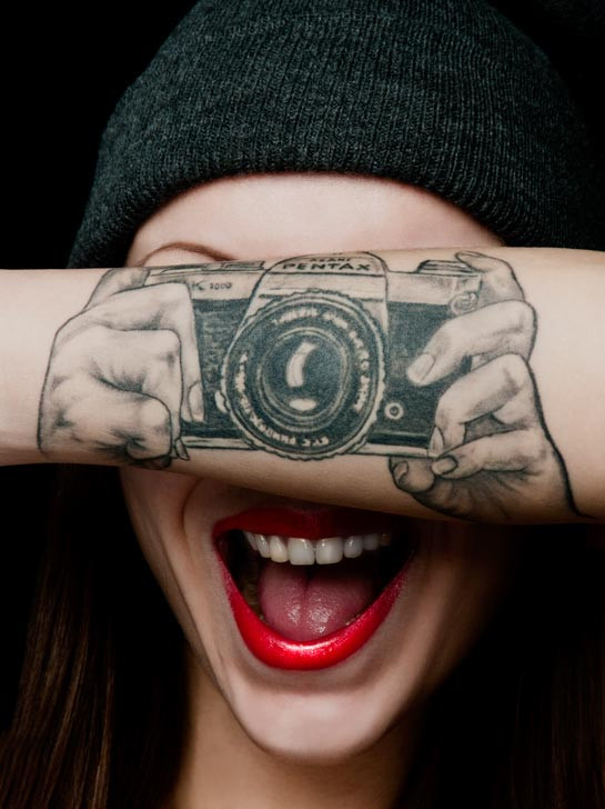 Close-up of a black ink optical illusion camera tattoo on a woman's arm