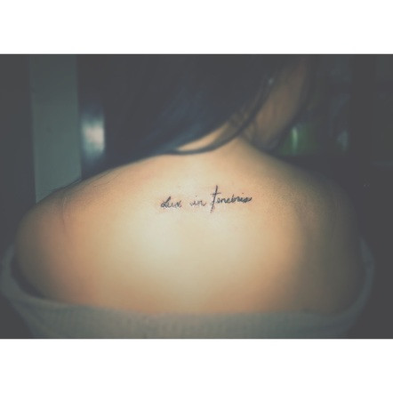 Lux in Tenebris phrase tattoo on collarbone, elegant font.