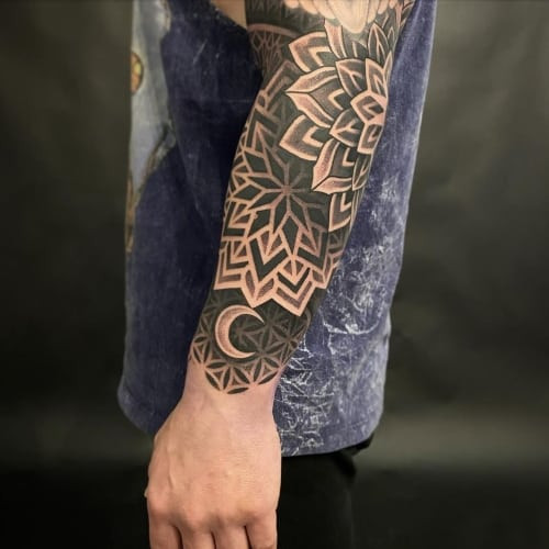 A mandala tattoo with intricate patterns on a man's arm, representing universe