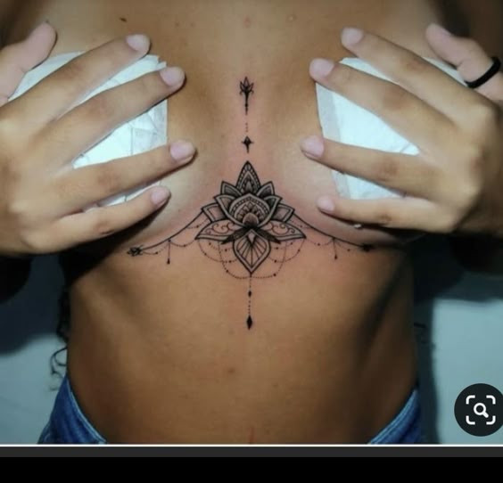 Underboob lotus tattoo with intricate designs, black ink art, covering the sternum area.