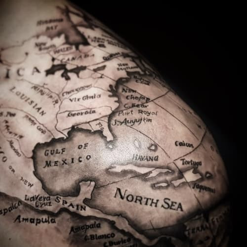 A world map tattoo with detailed continents on a man's arm, symbolizing travel passion