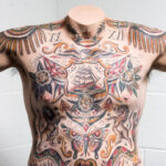 Sailor's torso with various tattoos, including a swallow, showcasing traditional naval ink.