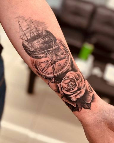 Forearm tattoo featuring a compass rose intertwined with a blooming rose, symbolizing direction, guidance, and the journey of life.